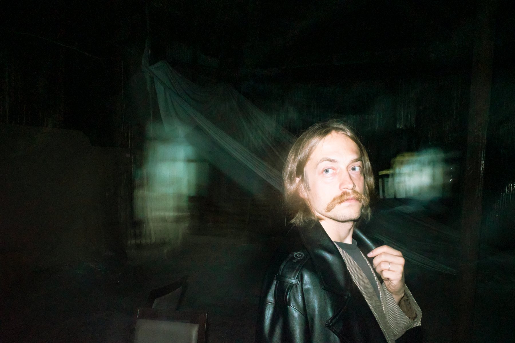 Niki in a leather coat, looking over his shoulder at night
